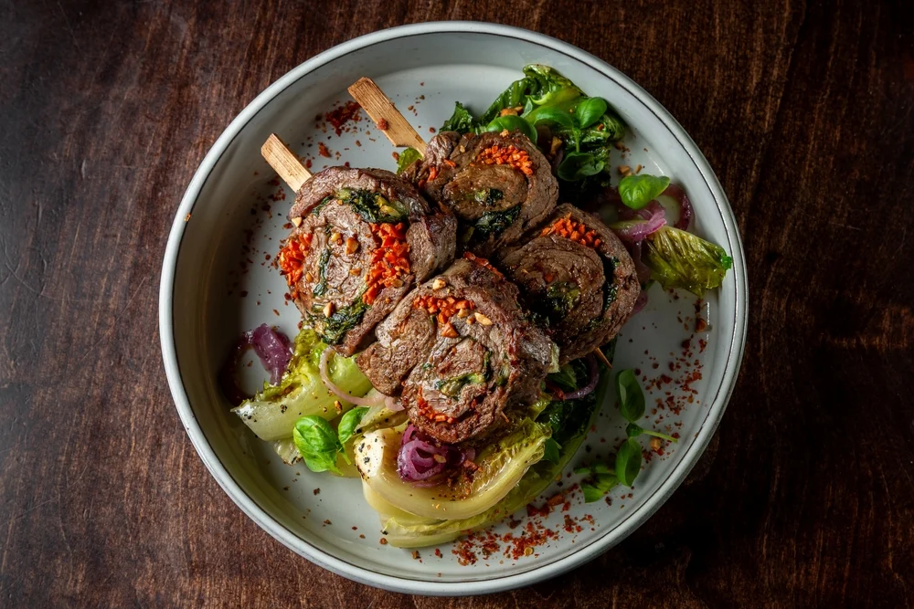 Tender beef rolls stuffed with vegetables, served on a plate with seasonal greens and garnished with spices.