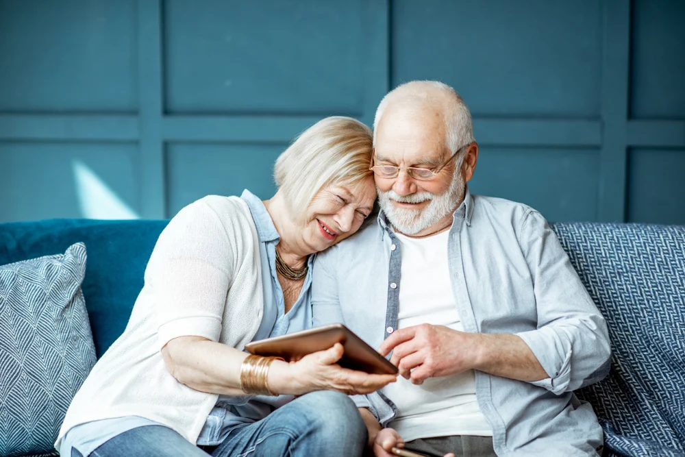 Senior couple enjoying time together while looking at a tablet on a cozy couch.